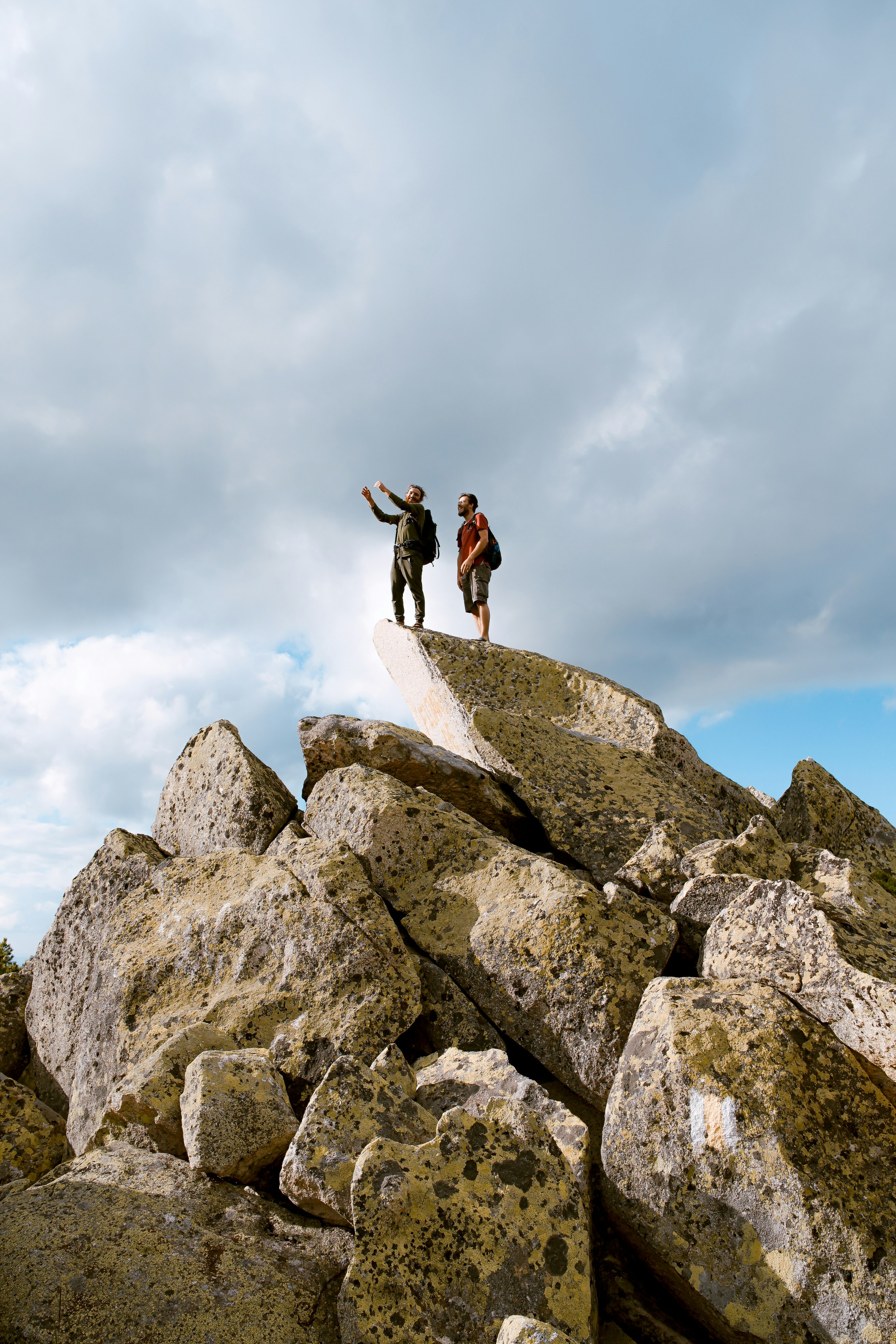two people standing on grey rock under white clouds